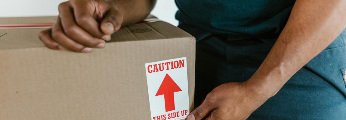 A smiling male mover in a blue shirt carries moving boxes in a truck.