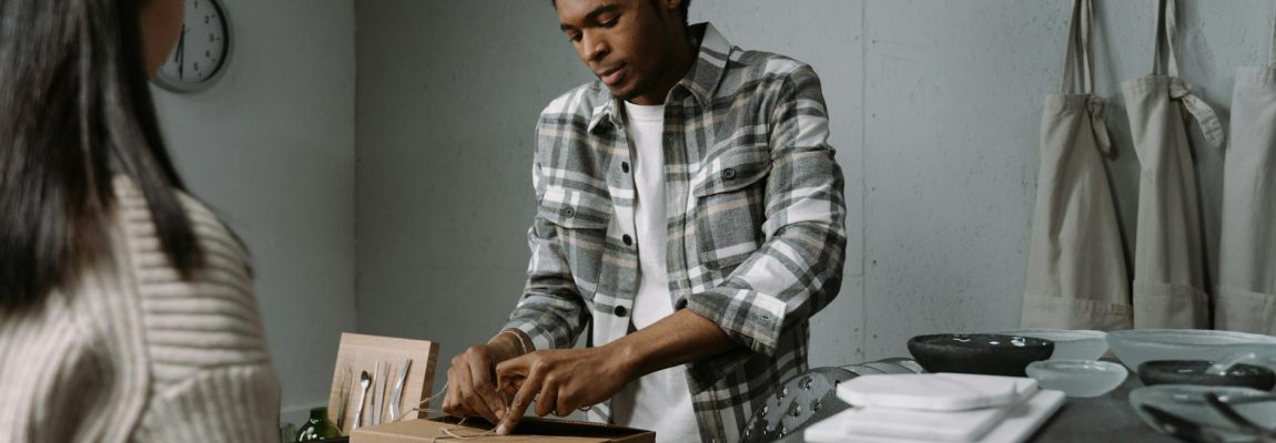 A smiling man in a red uniform carefully tapes a cardboard box in a moving truck.