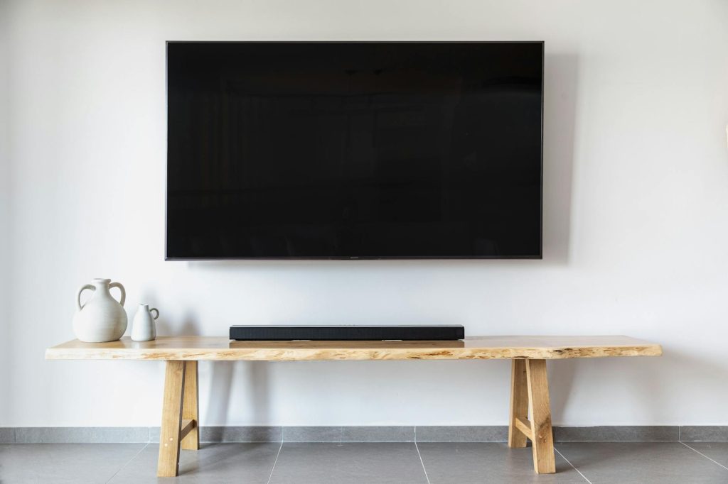 A mover in a yellow shirt holds a TV while standing on stairs, ready for wall mounting.