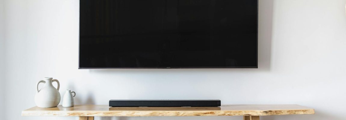Man installing a TV wall mount bracket in a living room, with tools on the floor nearby.