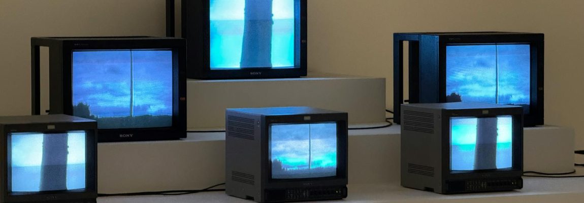 A professional installer mounting a flat-screen TV on a wall, with tools on a white shelf nearby.